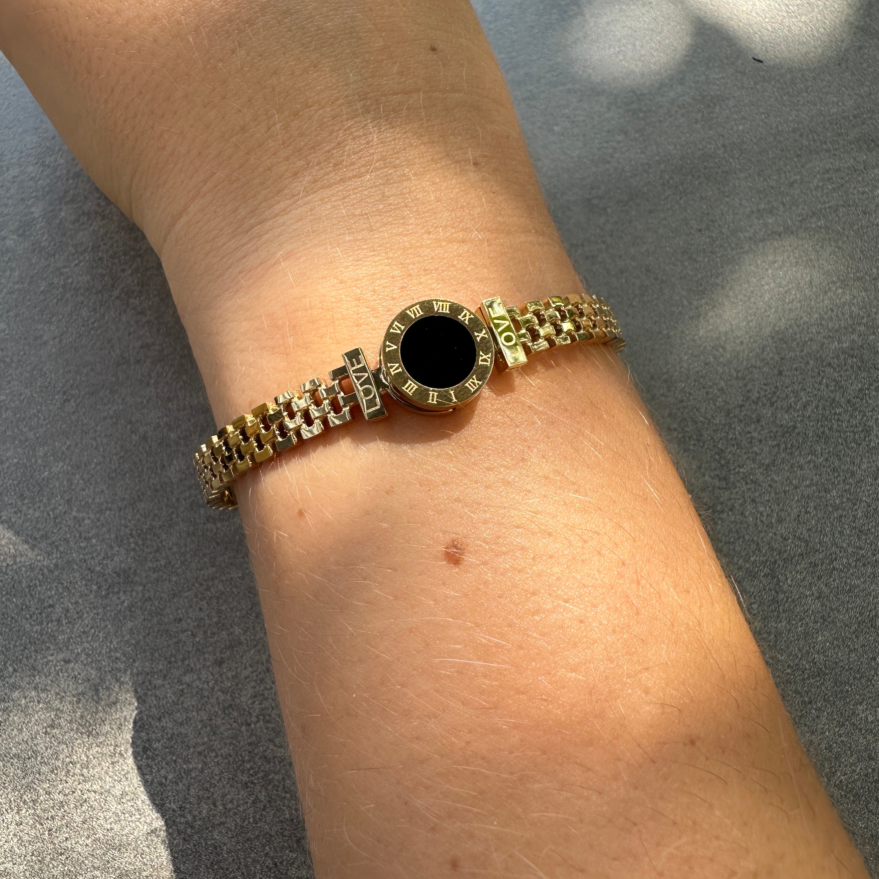 Gold bracelet with a black center on a wrist against a gray background